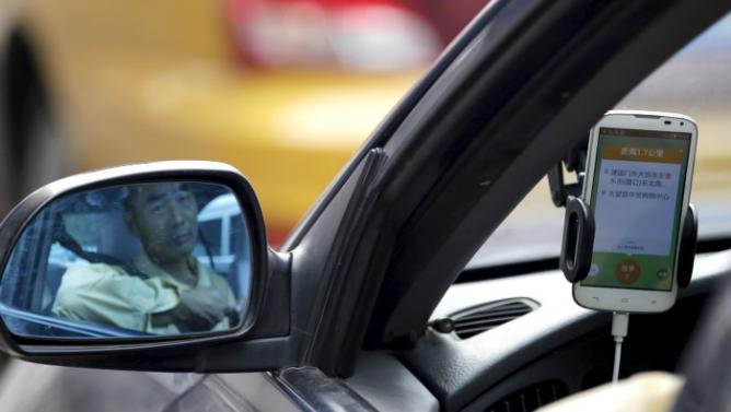 A taxi driver is reflected in a side mirror as he uses the Didi Chuxing car-hailing application in Beijing, China, September 22, 2015. REUTERS/Jason Lee