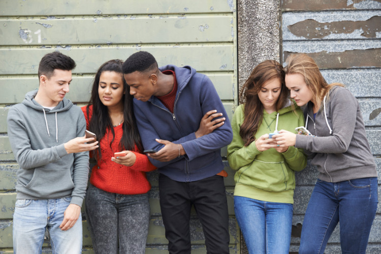 Group Of Teenagers Sharing Text Message On Mobile Phones